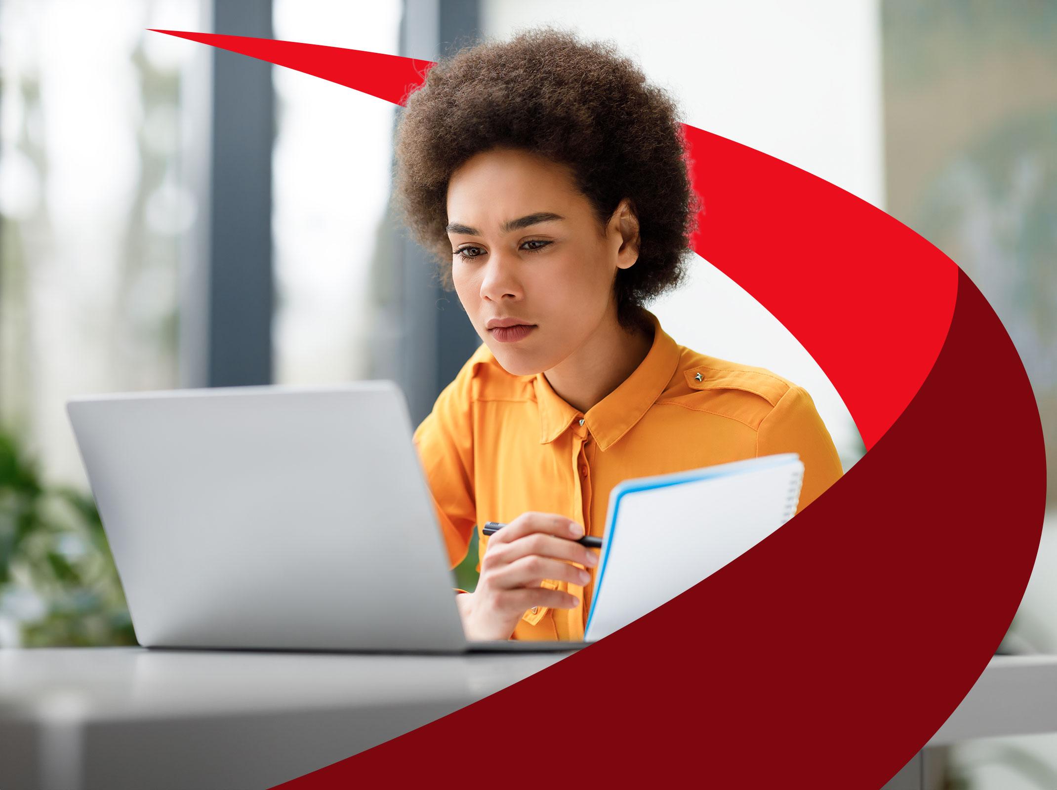 Woman looking at laptop and holding notebook
