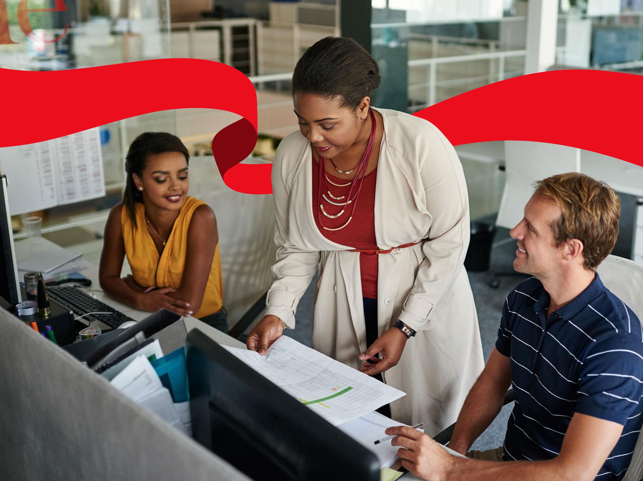 A business leader delegating items to two employees. She is sharing a document in front of computer screens.
