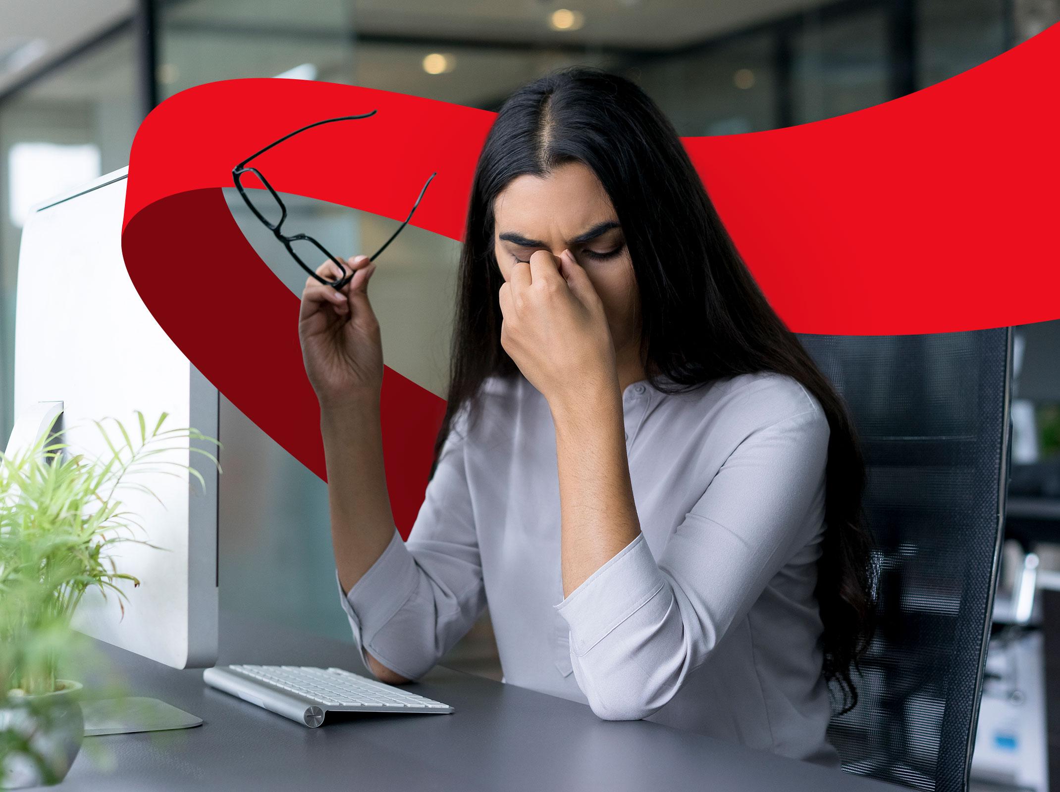 A female business professional with eyes closed pinching the bridge of her nose with her glasses in her other hand. She appears to be stressed in a business setting.
